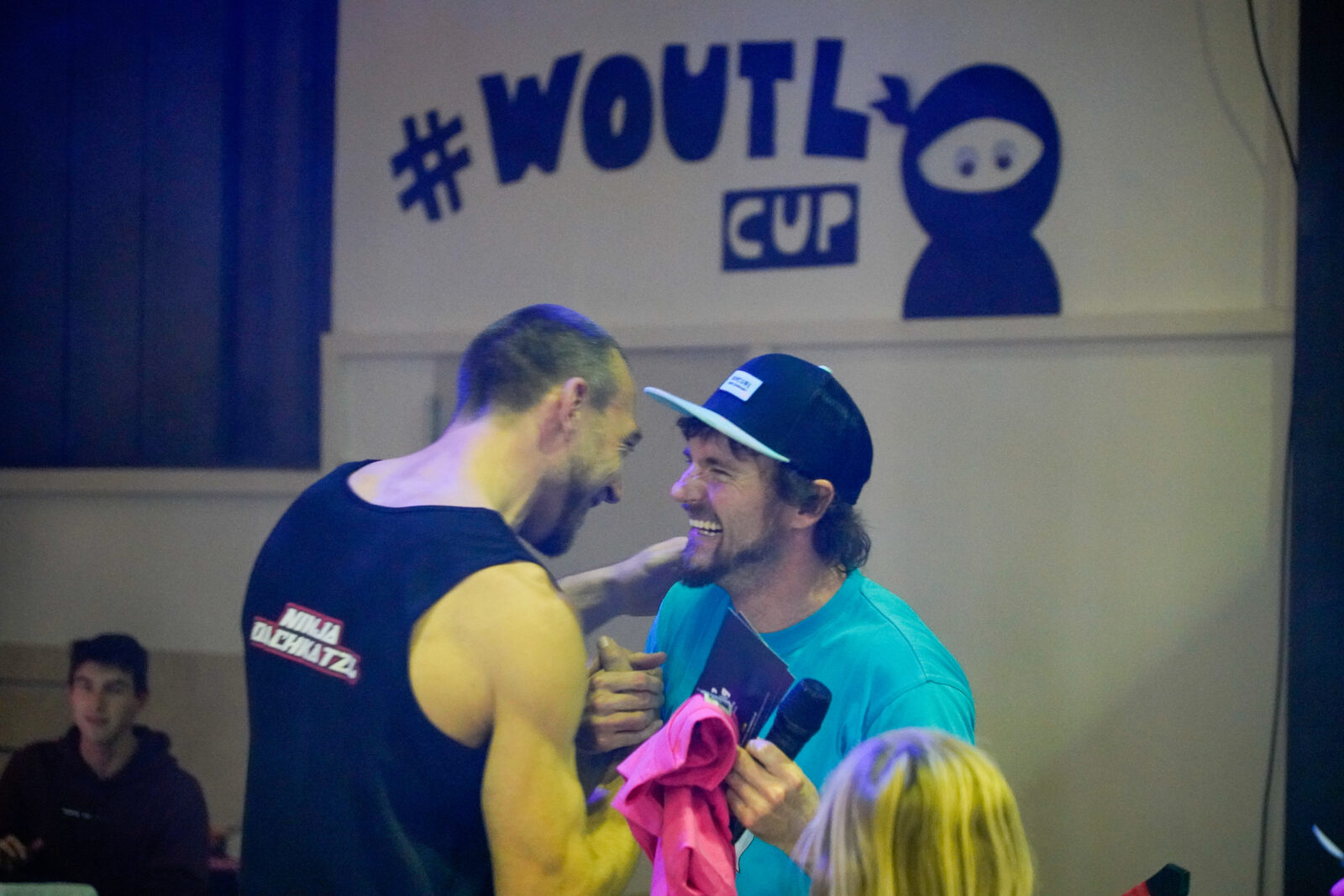 Zwei Athleten umarmen sich lachend unter dem Woutl-Cup-Logo